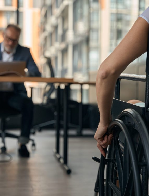 Close up of woman using wheelchair while going to interview with male collegue sitting at desk with notebook